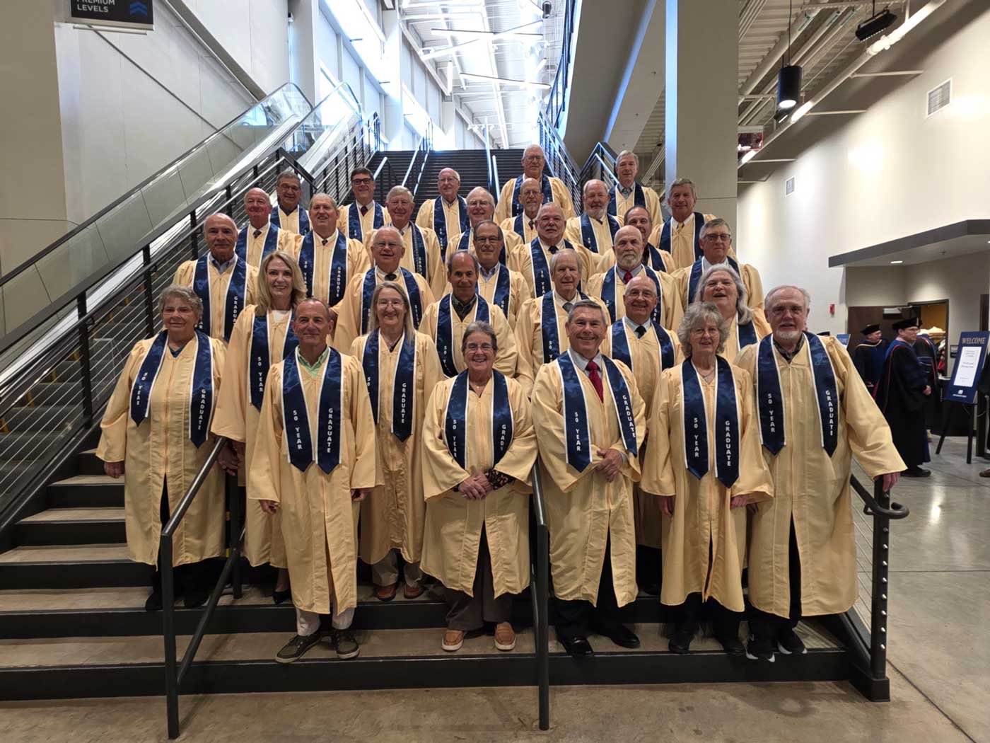 50-year-graduates-robes-web group of graduates wearing gold robes standing on stairs