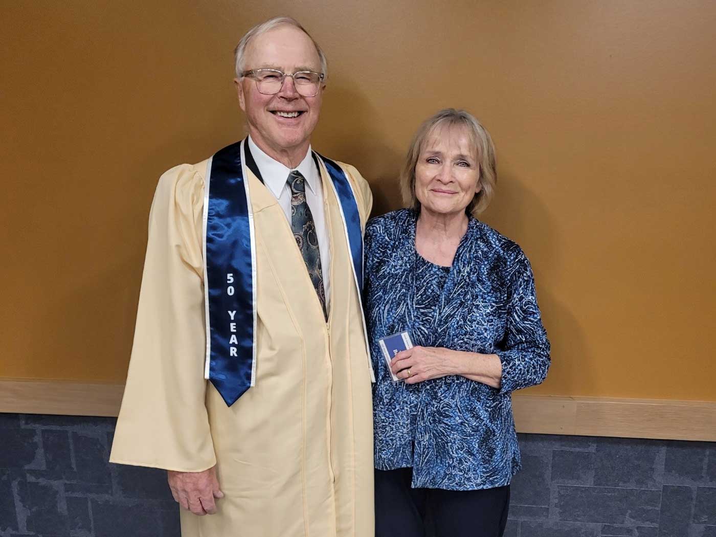 husband dressed in gold graduation gown with wife in blue shirt