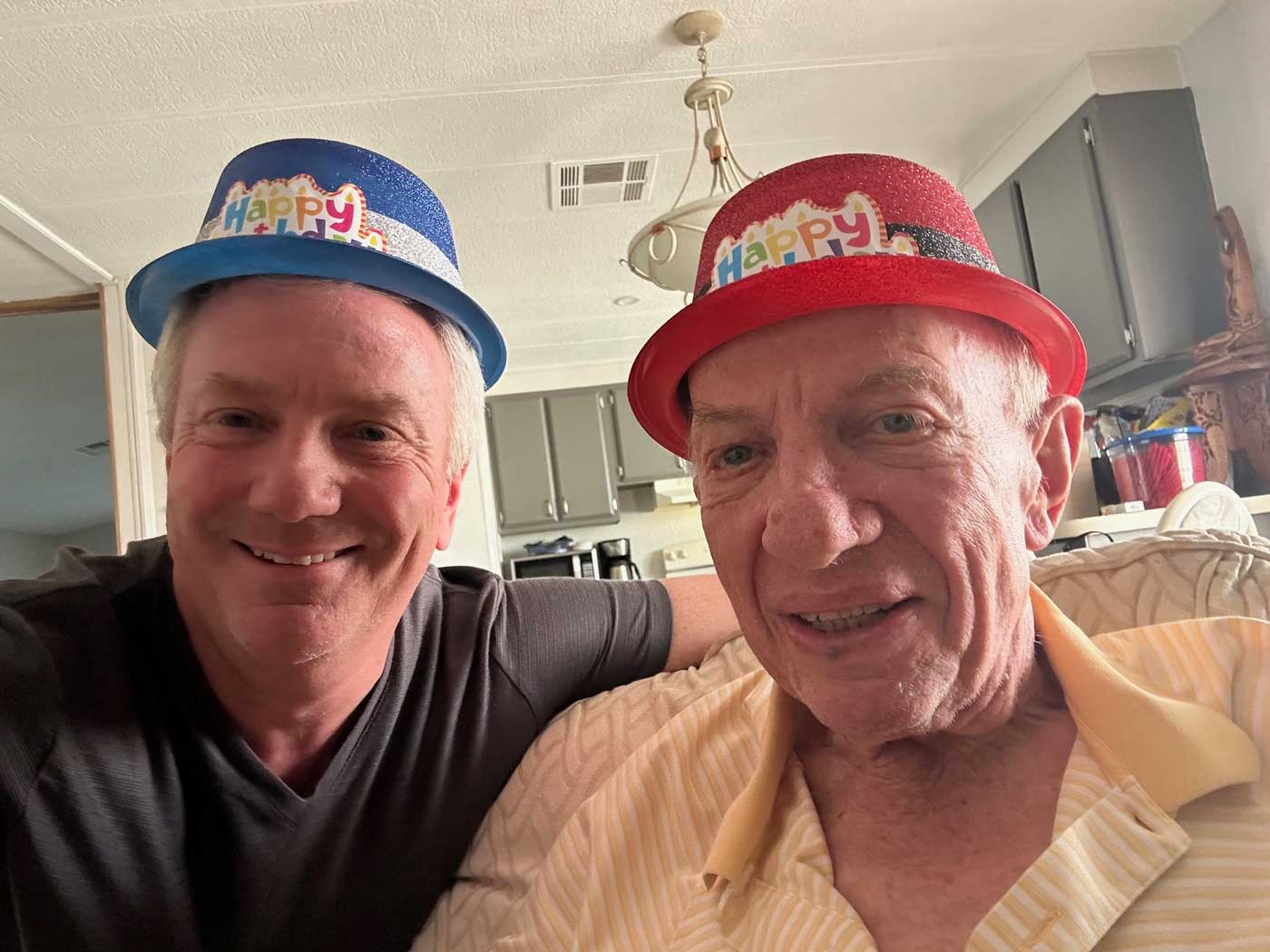 Bill-and-Dennis-Cullen-web two men smiling at camera wearing happy birthday hats