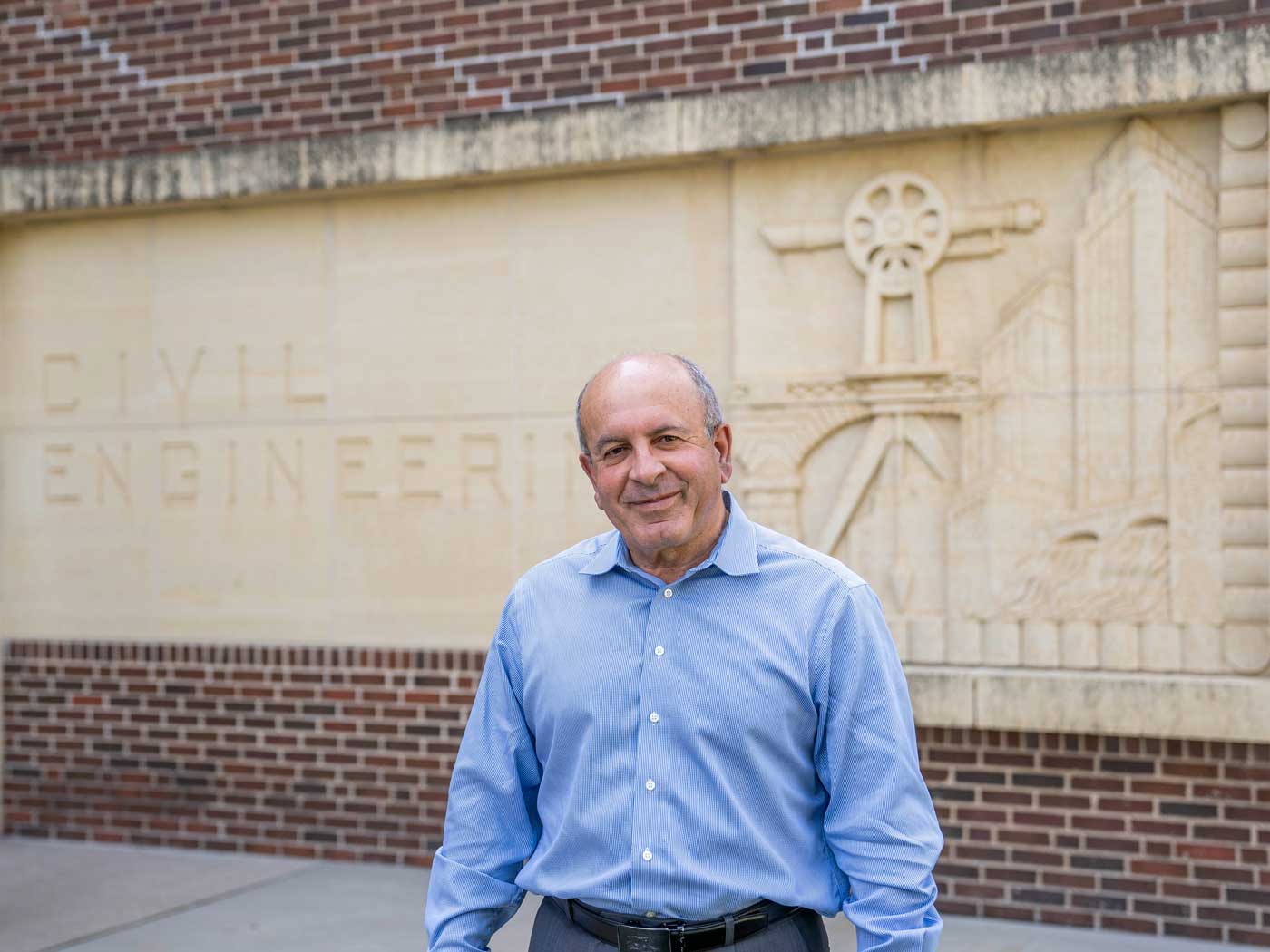 Hani-Shafai-web man wearing a blue button up shirt in front of a brick building