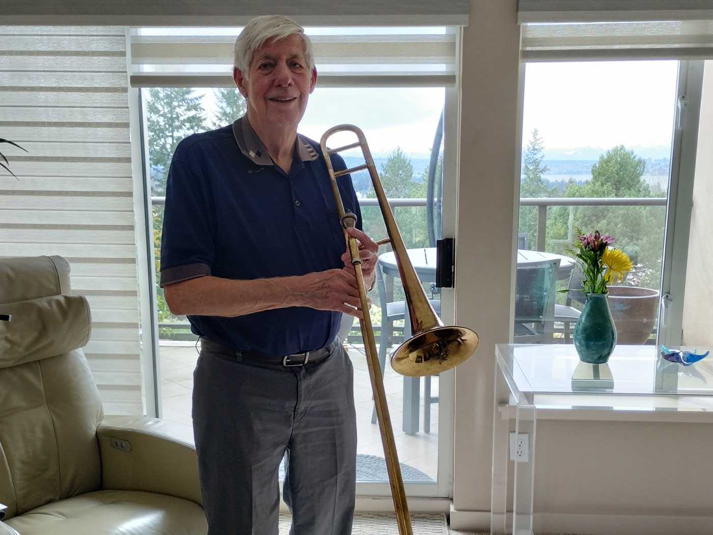 Jerry-DesJarlais-web man standing in living room holding trombone