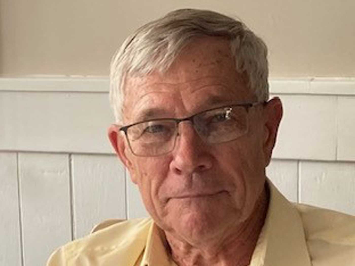 elderly man wearing yellow shirt in front of wall smiling at camera