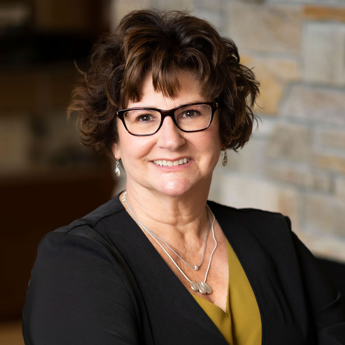 headshot of nancy beets wearing black blazer and yellow shirt