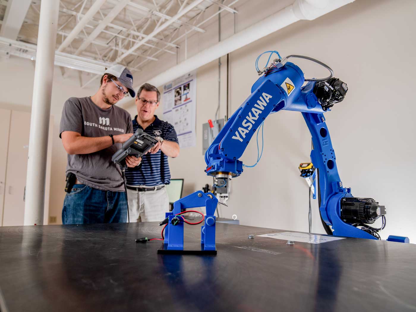 two men looking at a remote control and a robot arm