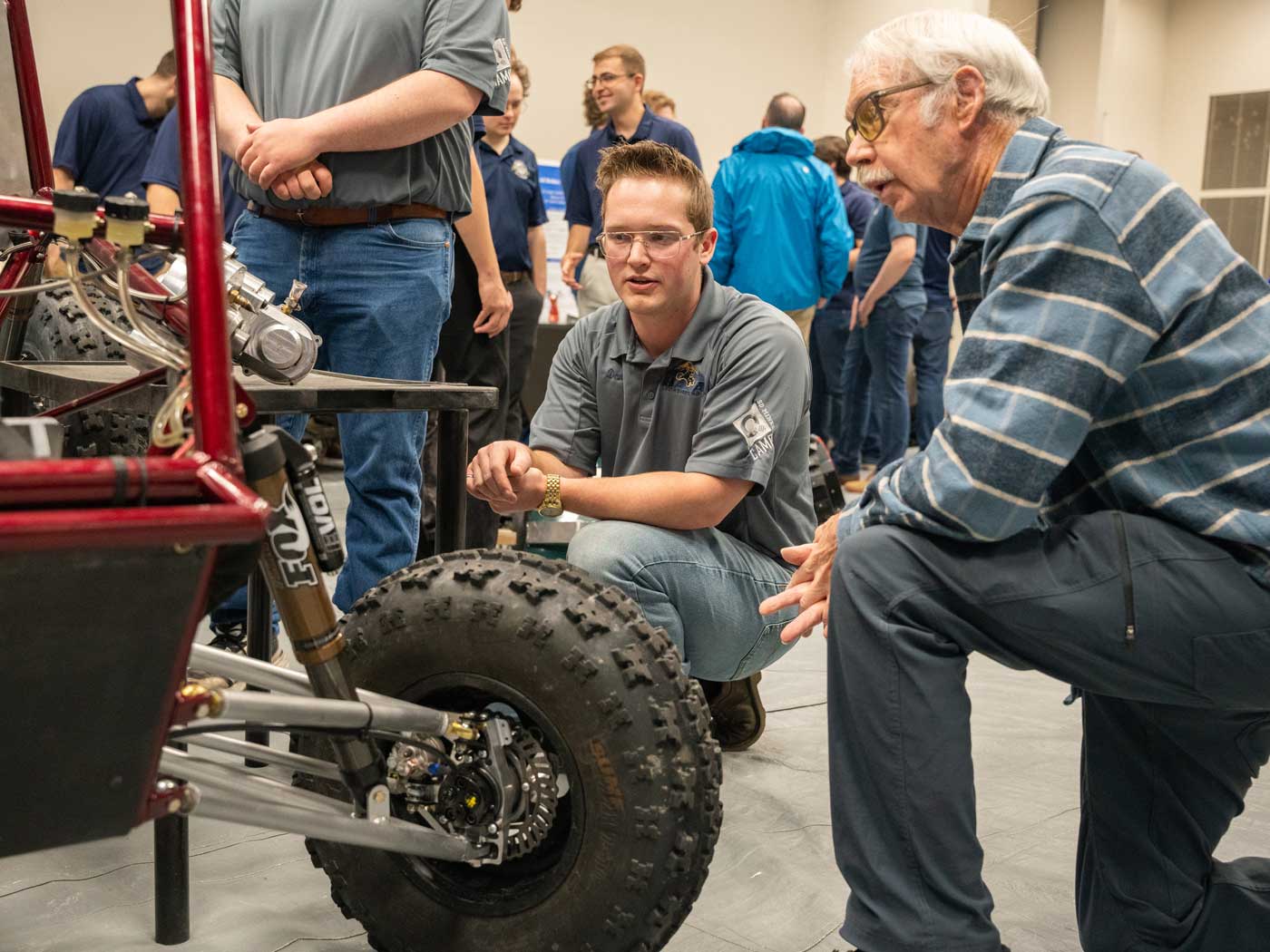 student and professor kneeling on ground looking at baja car