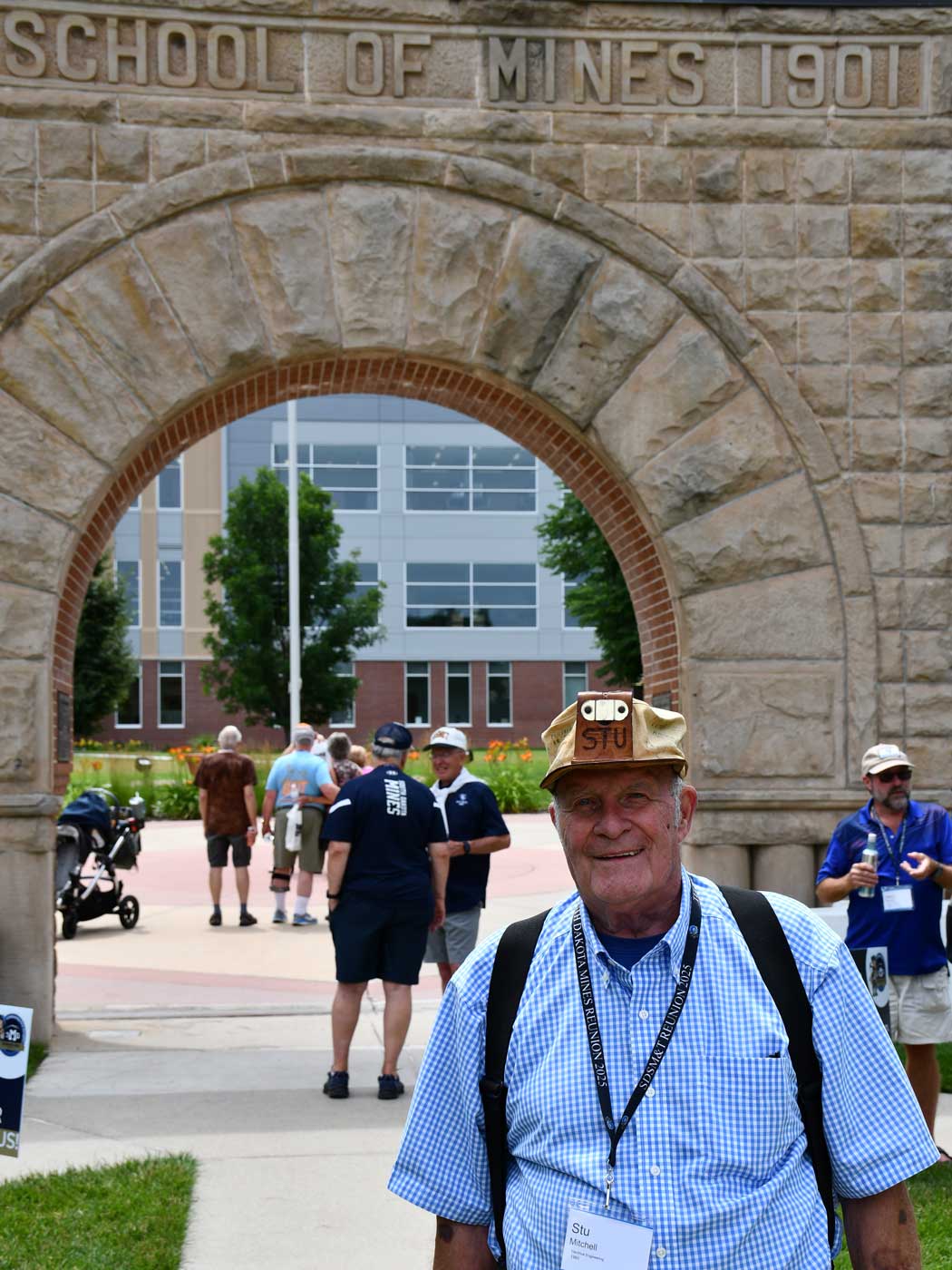 alumni wearing senior hat in front of arch in quad