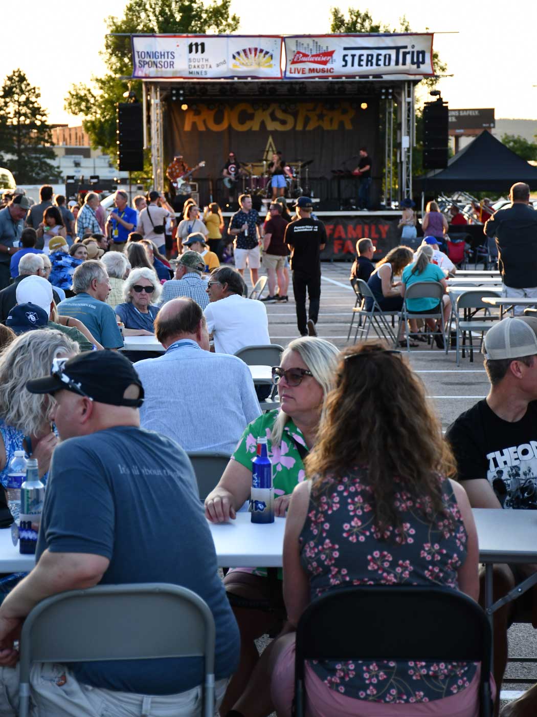 group of people at concert in parking lot with stage in background