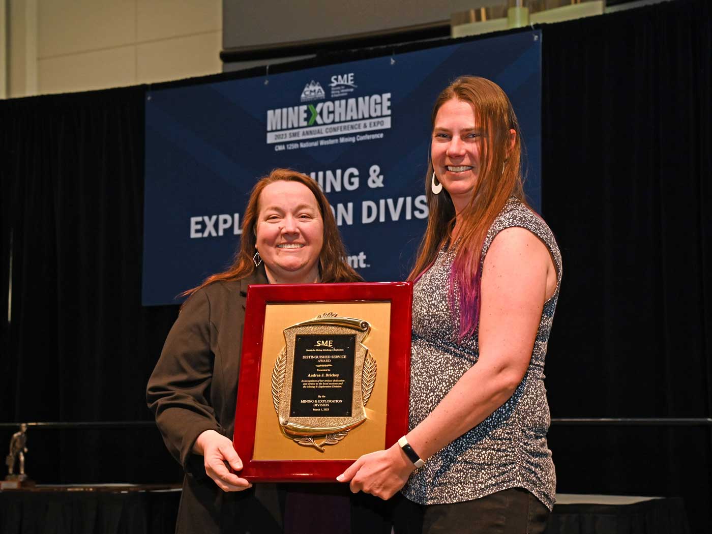 two women holding an award in front of a blue and black backdrop