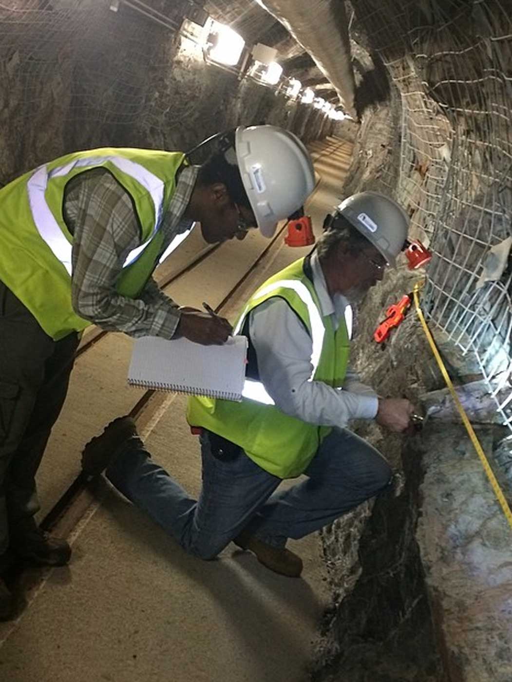 men wearing hard hats and reflective vests working inside of an underground mine