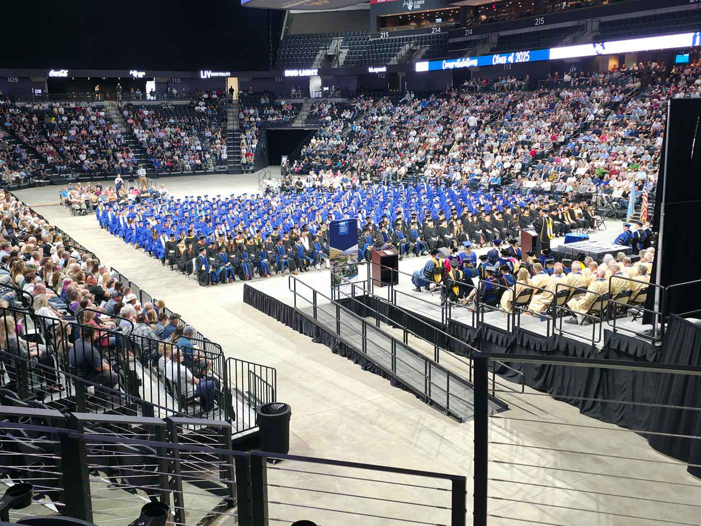 graduation ceremony with students in blue robes sitting on chairs looking at stage