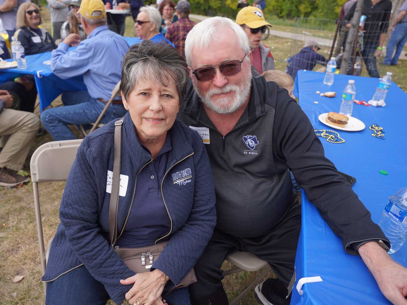 man and woman sitting at table with blue tablecloth at picnic