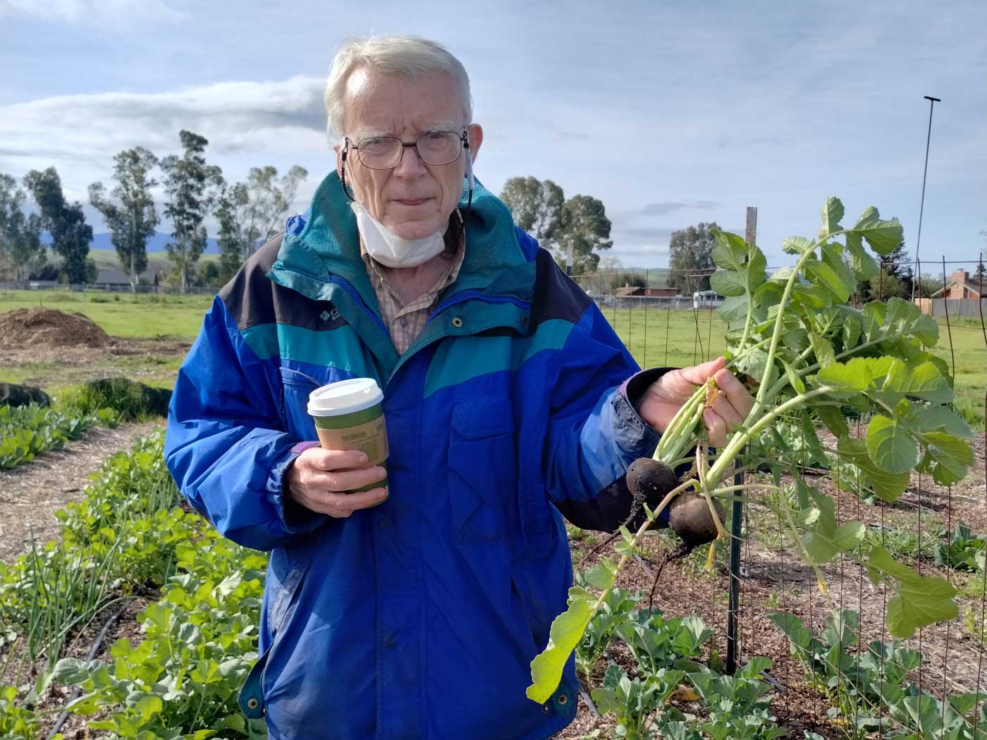 lance-sloan-web man holding coffee wearing a blue coat with plants in a garden