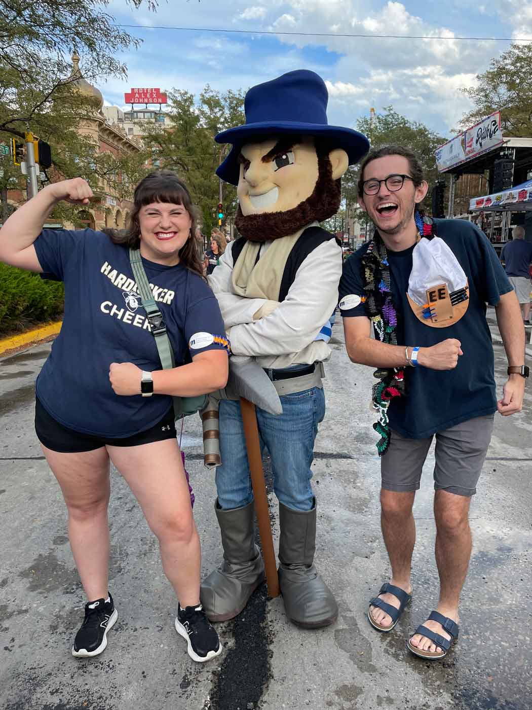 two students posing with Grubby the mascot in a street during a festival